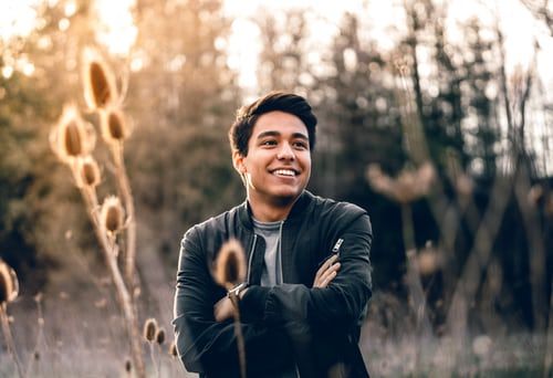 Smiling person with arms crossed, in a field, lit by the sun.